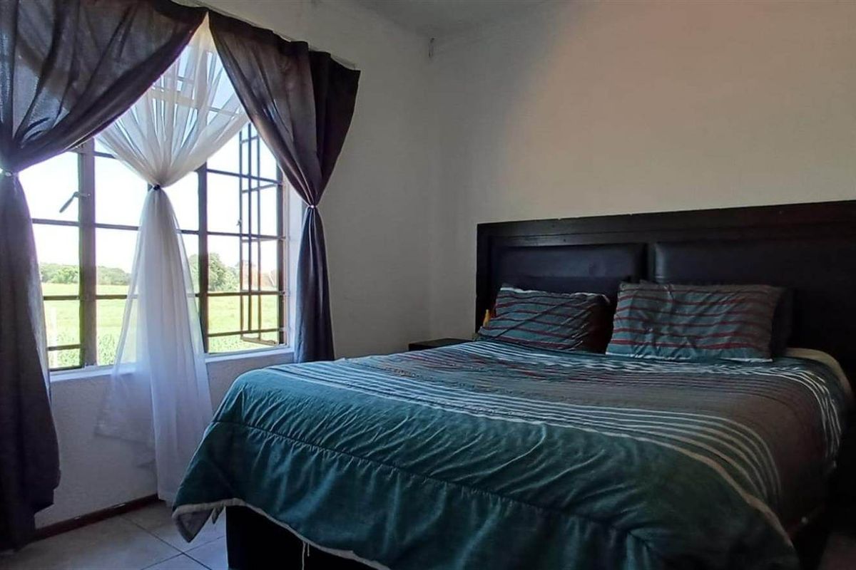 A functional bedroom featuring tiled flooring and a window fitted with security burglar bars, offering natural light and views.