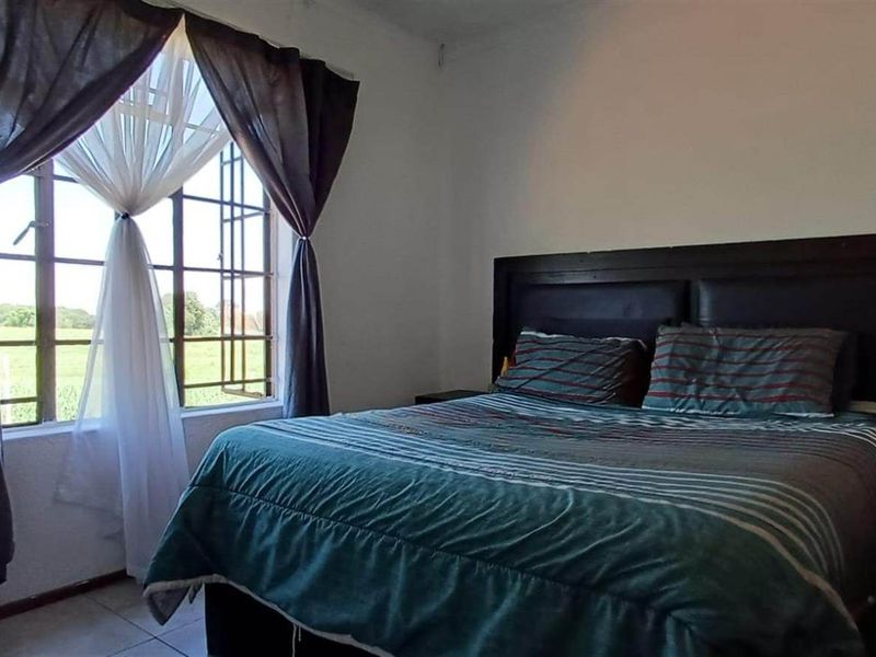A functional bedroom featuring tiled flooring and a window fitted with security burglar bars, offering natural light and views.