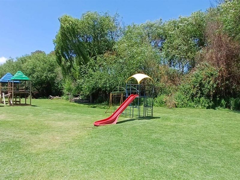 A spacious communal garden area featuring a well-maintained lawn and established playground equipment, surrounded by mature trees.