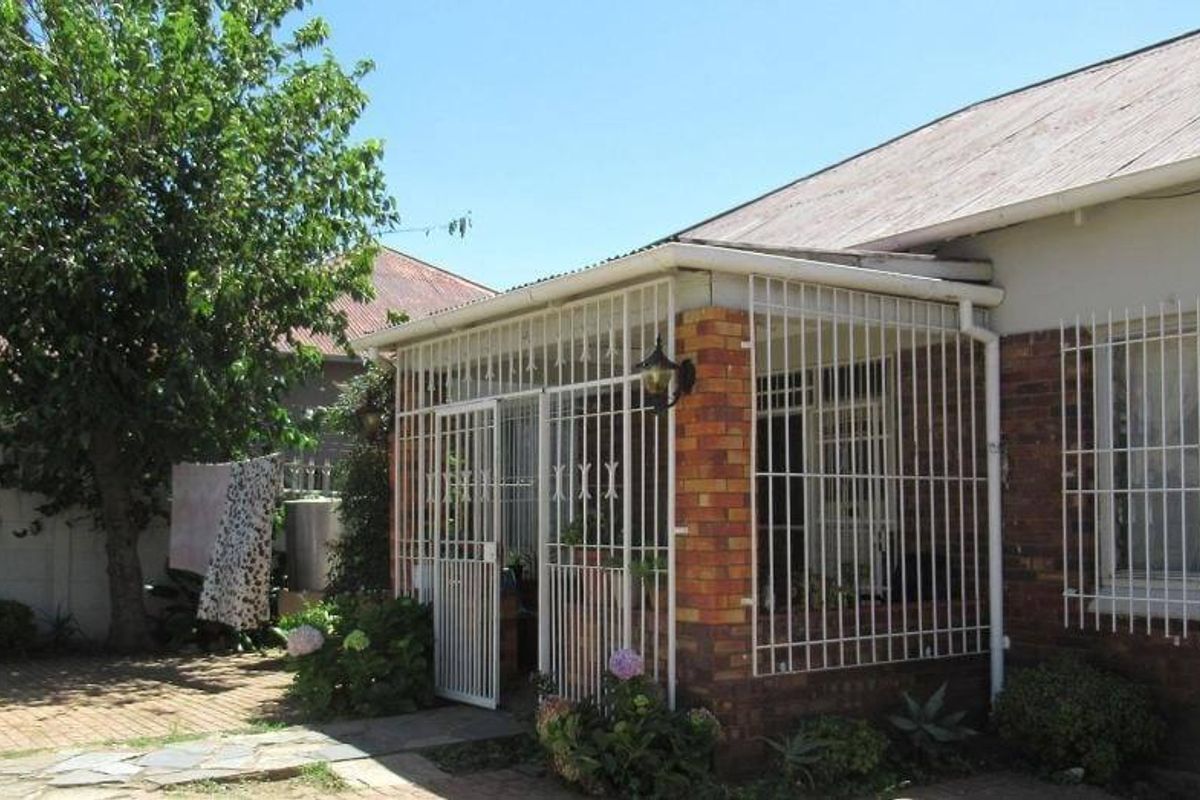 Rear view of the house featuring a paved patio area, brick exterior walls, and protective metal security bars on windows and the patio entrance.