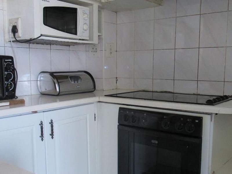 A compact kitchen featuring built-in oven, electric hob, microwave, and tiled backsplash with white cabinetry and laminate countertops.