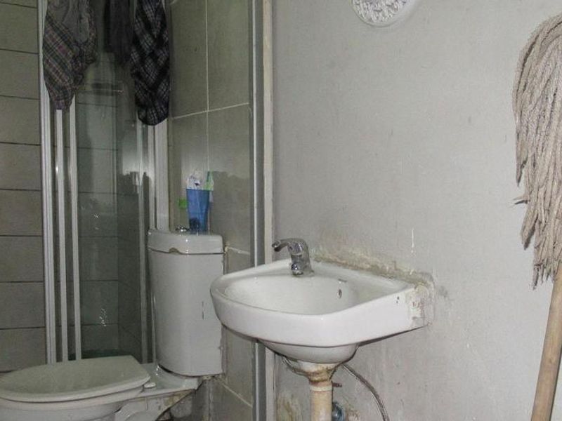 A small bathroom featuring a shower enclosure, toilet, and wall-mounted basin, currently in need of significant maintenance and cosmetic updates.