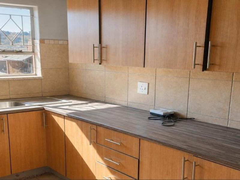 A functional kitchen featuring wood-finish cabinetry, laminate countertops, a stainless steel double sink, and tiled backsplash with natural light from the window.