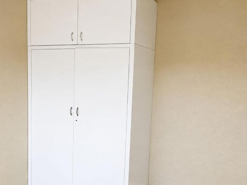 A clean, empty bedroom featuring a white built-in wardrobe with overhead storage and neutral wall finishes.