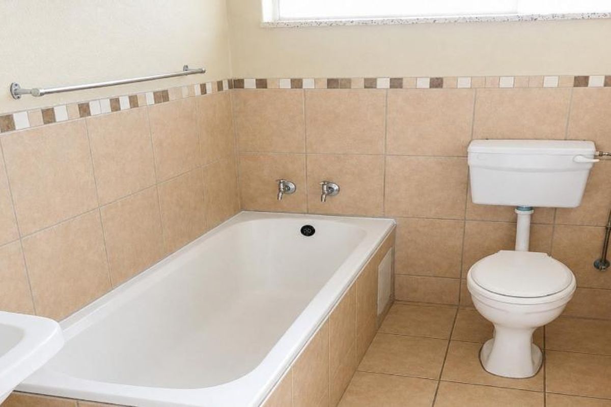 A functional bathroom featuring a bathtub, toilet, and washbasin with neutral wall and floor tiling.