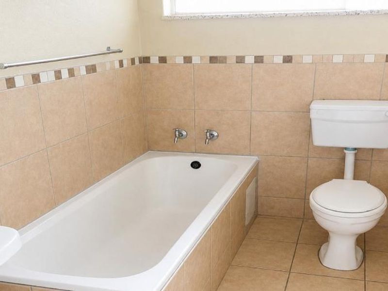 A functional bathroom featuring a bathtub, toilet, and washbasin with neutral wall and floor tiling.