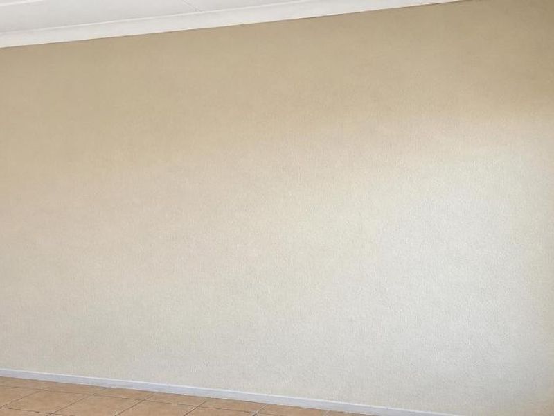 A clean, empty bedroom featuring neutral walls, tiled flooring, and a built-in cupboard, offering a blank canvas for personalization.