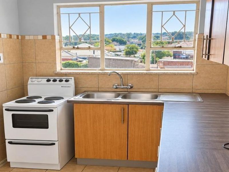 A functional kitchen featuring tiled splashbacks, laminate countertops, a double sink, and a freestanding stove, with natural light from a window overlooking the neighborhood.