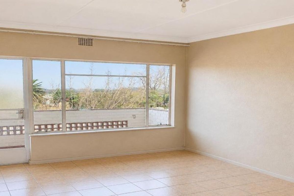 A bright, empty living room featuring tiled flooring, a large window with natural light, and access to an outdoor balcony area.