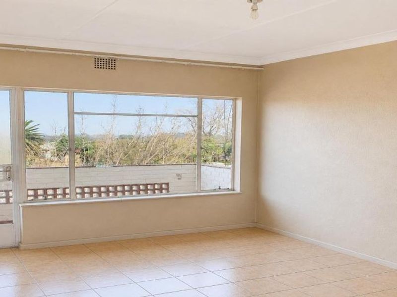 A bright, empty living room featuring tiled flooring, a large window with natural light, and access to an outdoor balcony area.