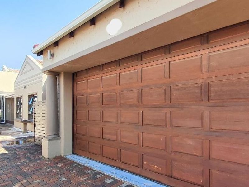 Side view of the property featuring a wooden garage door, paved driveway, and a structural column leading toward the rear garden area.