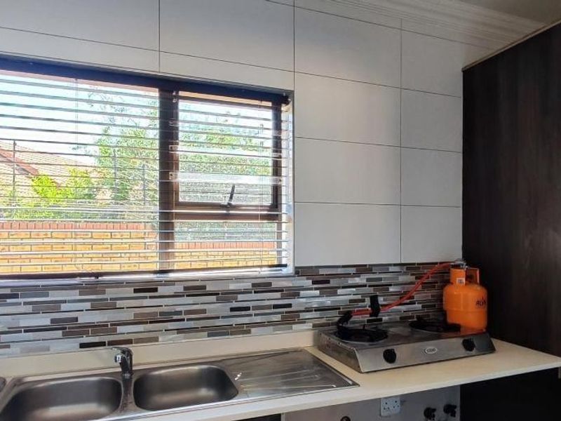 A functional kitchen area featuring a double stainless steel sink, mosaic tile backsplash, and ample built-in cabinetry with modern wall tiling.