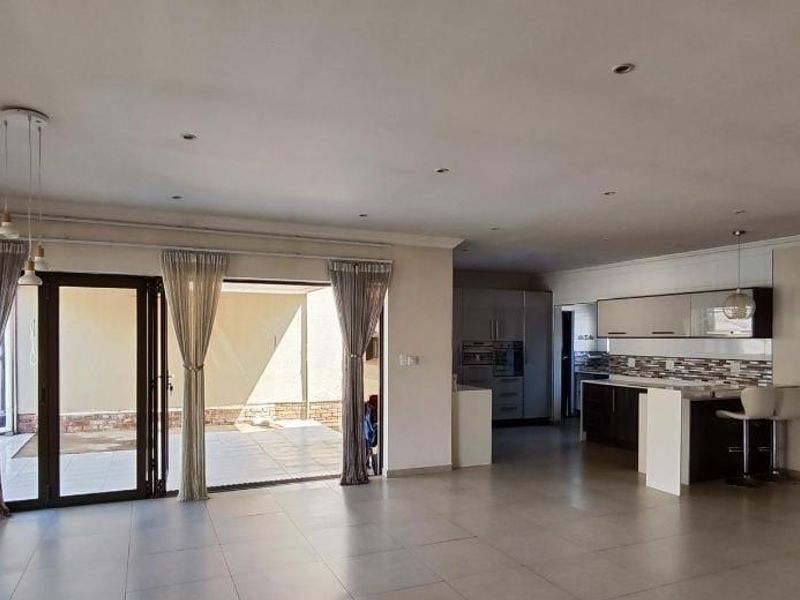 Spacious open-plan living area featuring tiled floors, recessed lighting, and a modern kitchen with built-in cabinetry, flowing seamlessly to an outdoor patio.