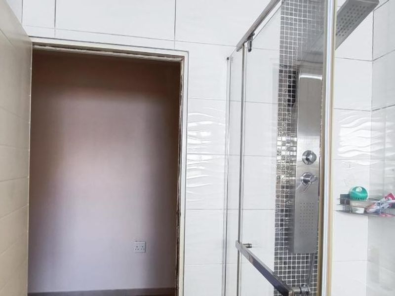 A bathroom featuring a glass shower enclosure with a modern shower panel and white wall tiling, requiring minor finishing touches to the door frame.