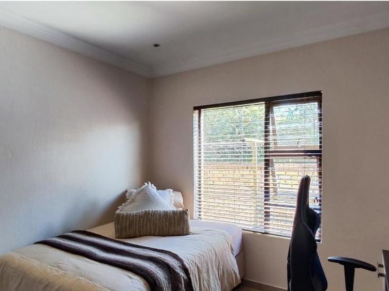 A functional bedroom featuring neutral walls, coving, and a window fitted with venetian blinds, providing natural light and a view of the exterior.