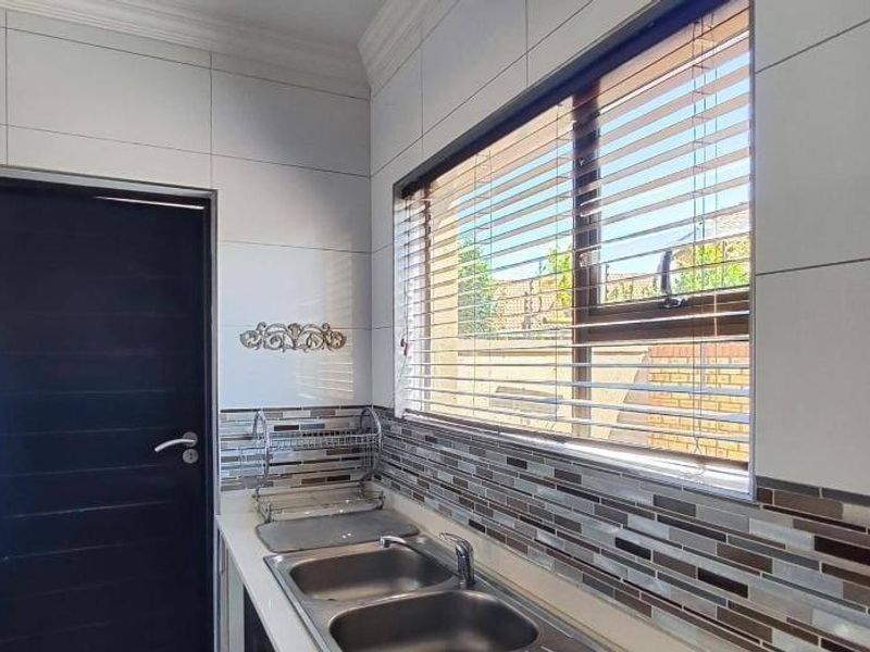 A clean and functional scullery area featuring a double stainless steel sink, modern tiled splashback, and large window with venetian blinds.