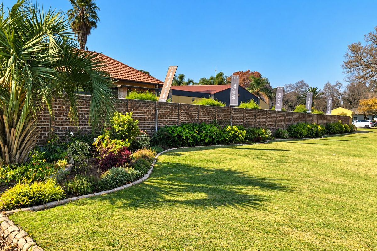 A well-maintained commercial garden area featuring a manicured lawn, landscaped garden beds with stone edging, and a long brick boundary wall.