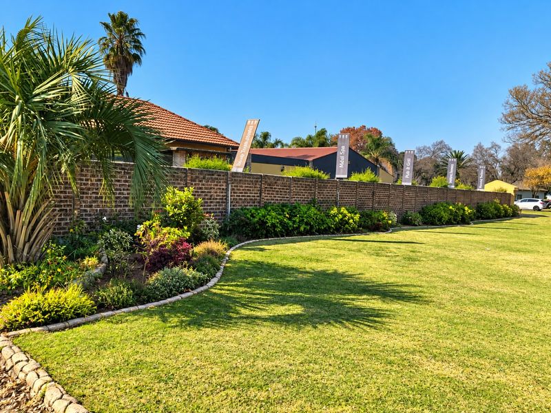 A well-maintained commercial garden area featuring a manicured lawn, landscaped garden beds with stone edging, and a long brick boundary wall.