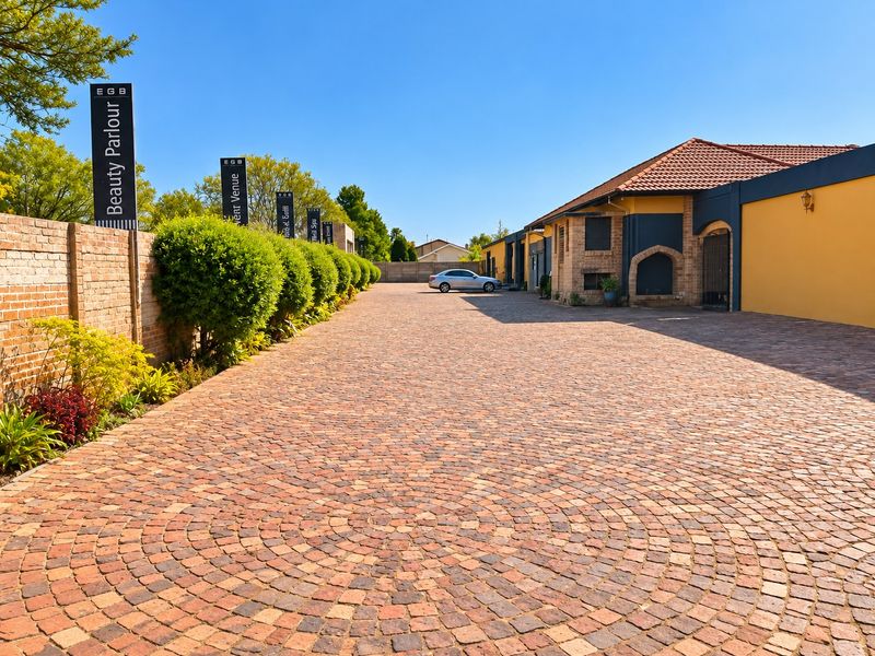 A well-maintained commercial property entrance featuring a circular pattern cobblestone driveway, brick boundary wall, and landscaped hedging leading to the main building.