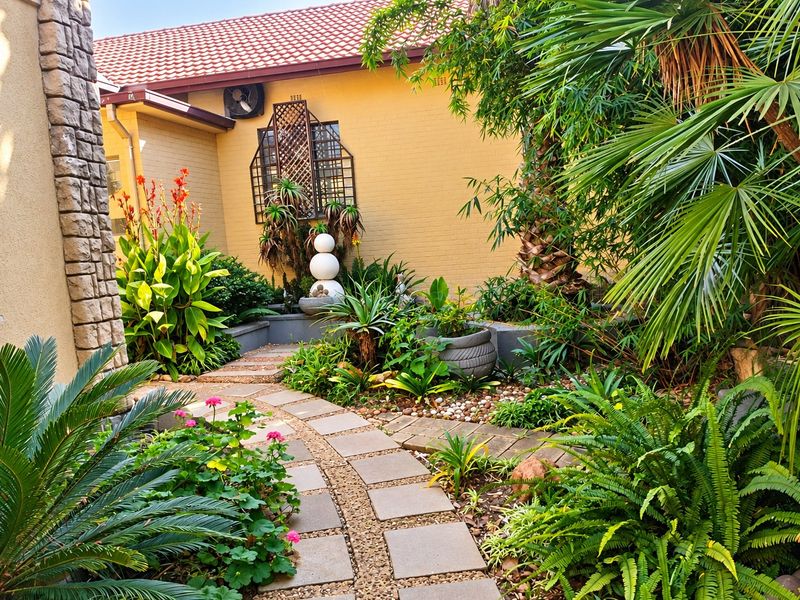 A well-maintained landscaped garden featuring a stone-paved pathway, lush greenery, and decorative plantings alongside the building exterior.