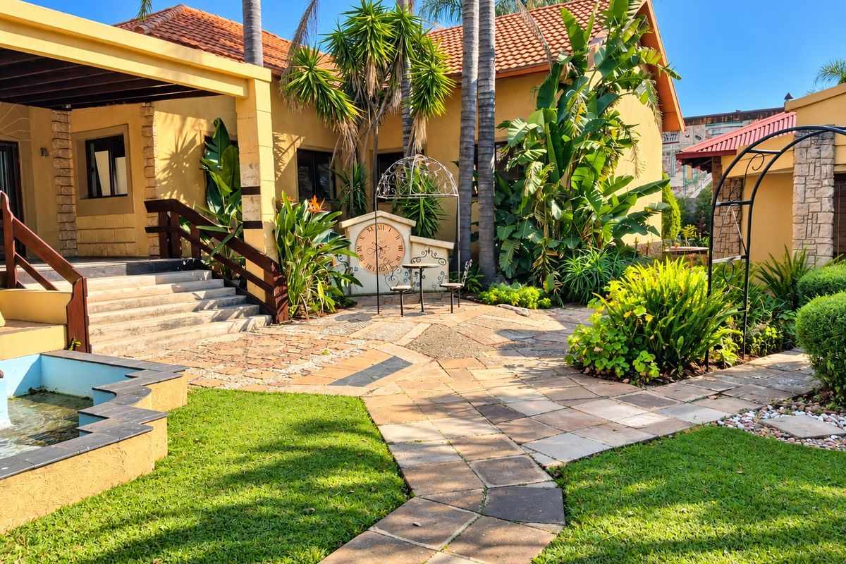 A well-maintained rear garden area featuring a stone-paved walkway, a built-in water feature, and a covered patio with timber stairs.