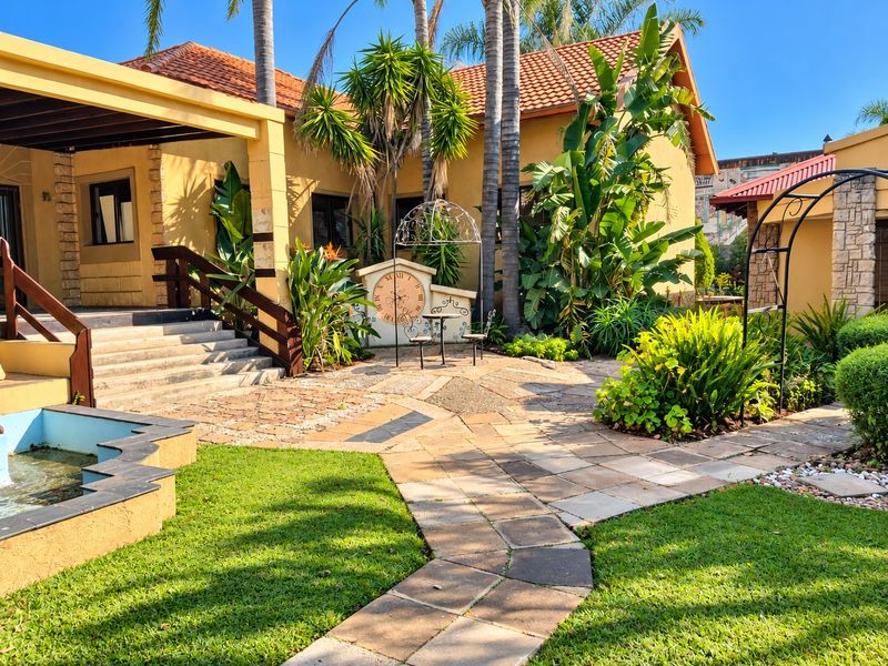 A well-maintained rear garden area featuring a stone-paved walkway, a built-in water feature, and a covered patio with timber stairs.