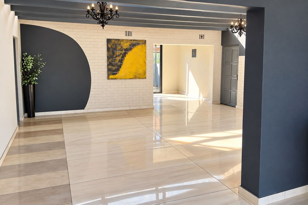 Spacious open-plan living area featuring polished porcelain tiles, exposed ceiling beams, and a modern brick feature wall with contemporary lighting.