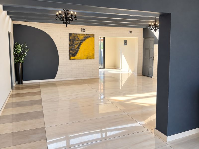 Spacious open-plan living area featuring polished porcelain tiles, exposed ceiling beams, and a modern brick feature wall with contemporary lighting.