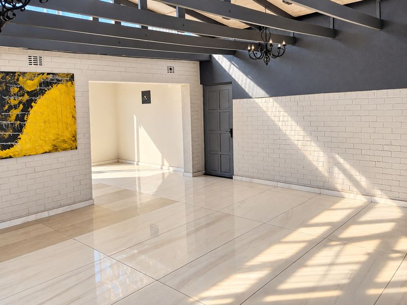 Spacious, light-filled living area featuring polished porcelain tiles, exposed timber ceiling beams, and modern painted brick walls, offering a clean, contemporary aesthetic.