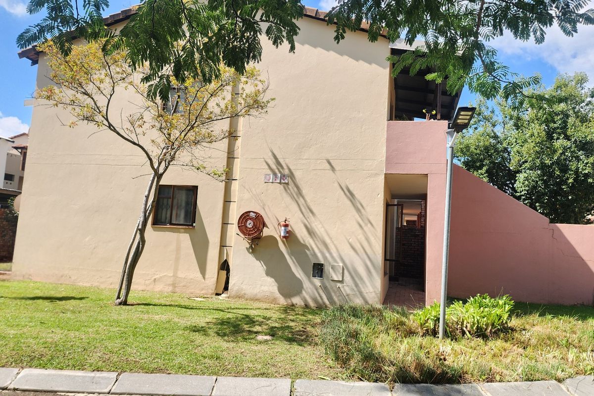 Rear exterior view of the apartment building featuring a paved walkway, fire safety equipment, and landscaped garden area.