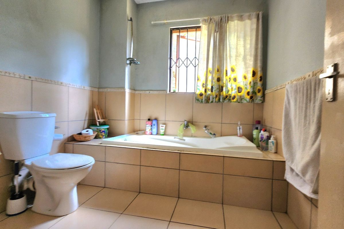 A functional bathroom featuring a built-in bathtub, toilet, and neutral wall and floor tiling with a window for natural light.