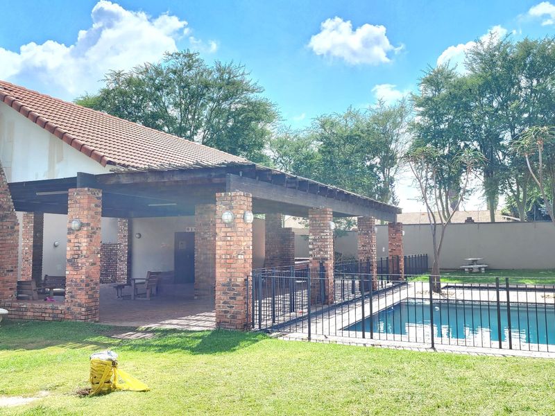Outdoor entertainment area featuring a covered brick patio, a swimming pool with metal safety fencing, and a large brick chimney structure.