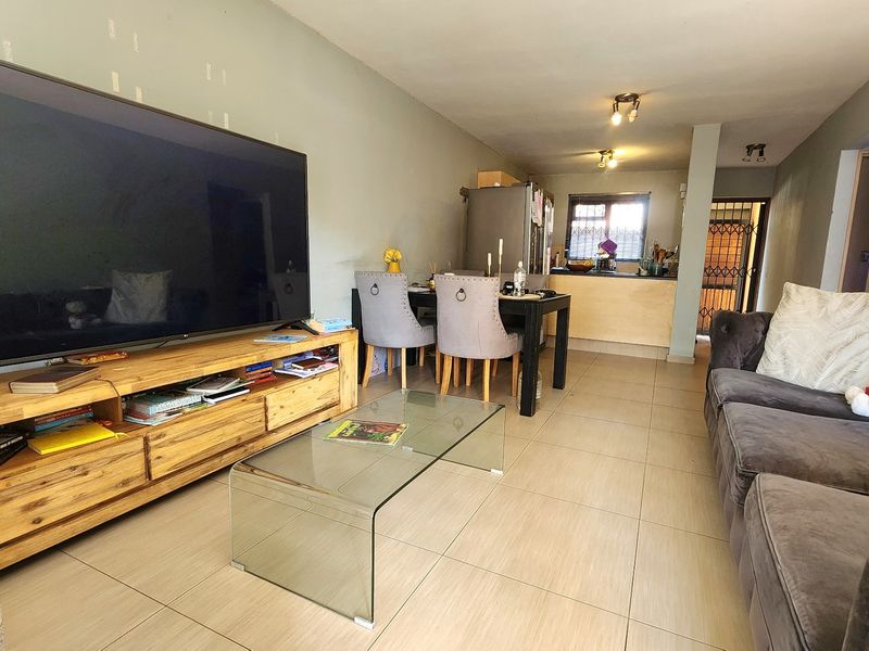 Open-plan living and dining area featuring tiled flooring, recessed lighting, and a connected kitchen space with a security gate at the entrance.