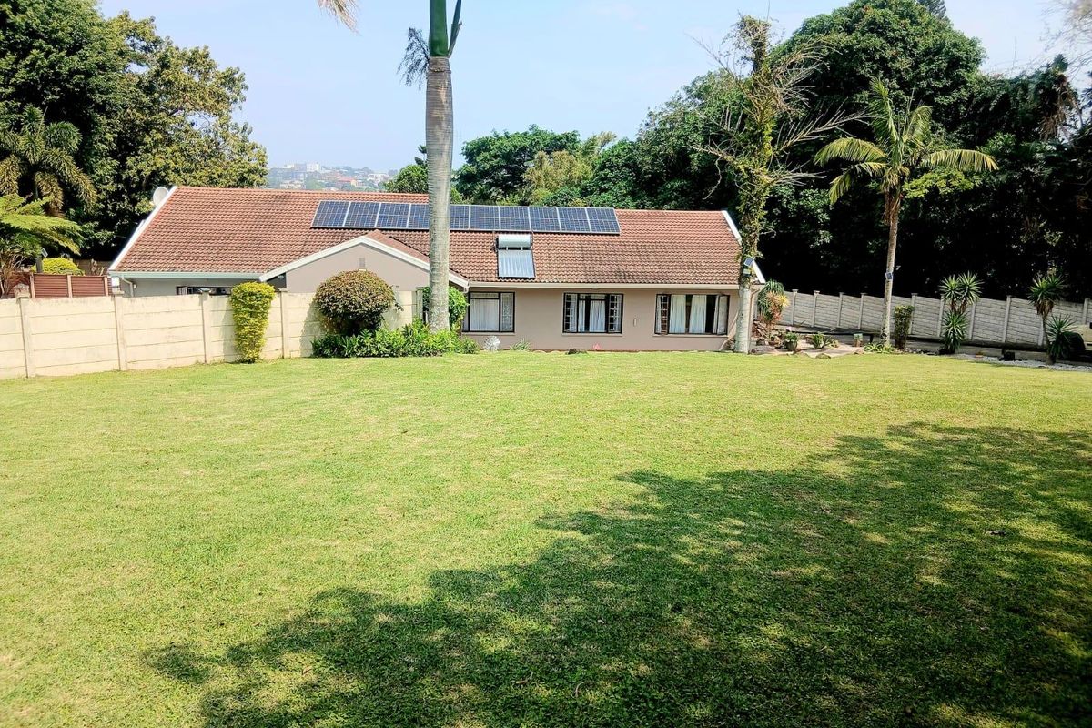 Spacious rear garden featuring a well-maintained lawn, precast boundary walls, and a house roof equipped with solar panels and a solar water heater.