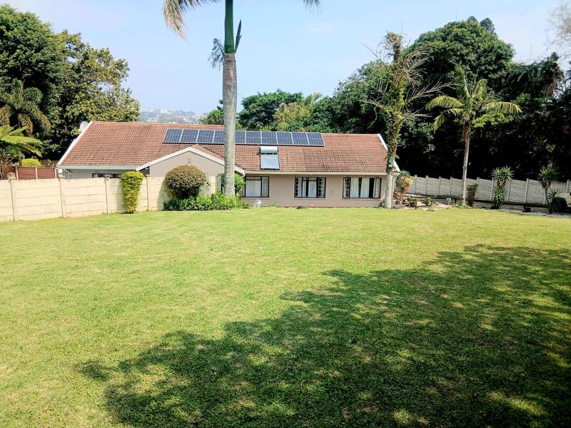 Spacious rear garden featuring a well-maintained lawn, precast boundary walls, and a house roof equipped with solar panels and a solar water heater.
