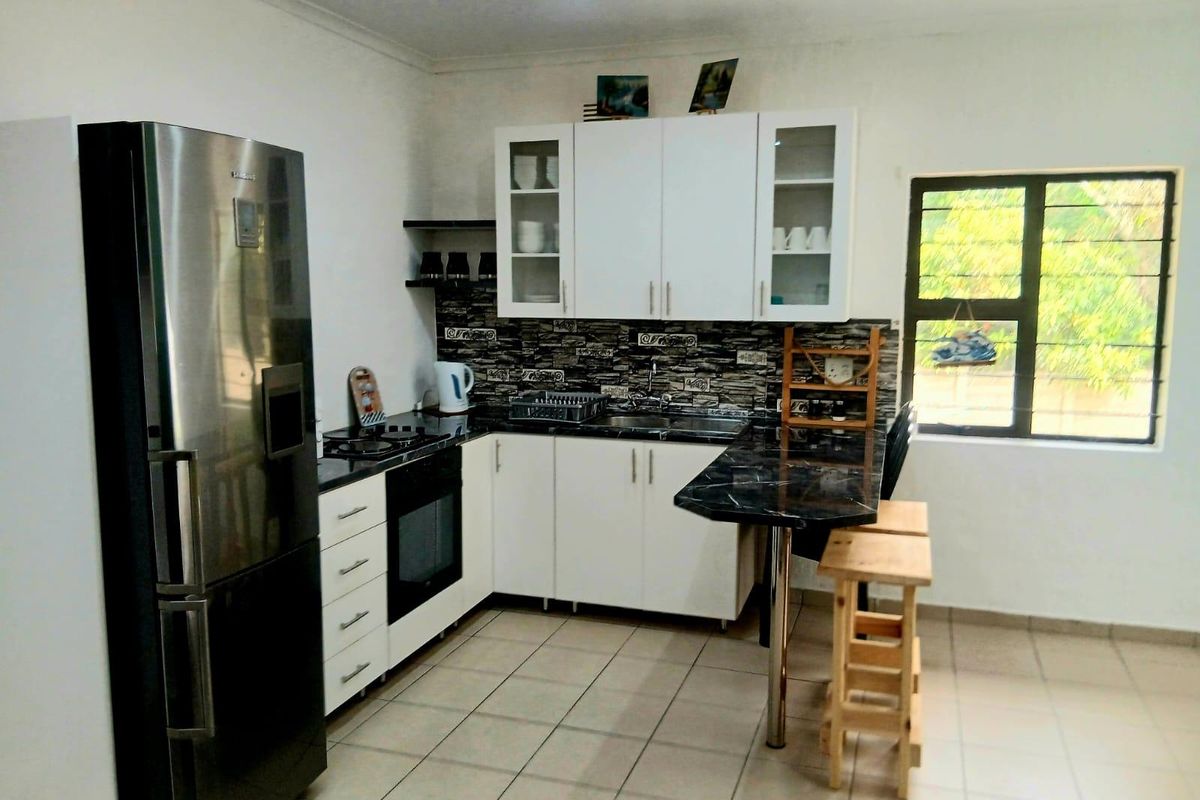 A functional kitchen featuring white cabinetry, dark stone countertops, a built-in oven, hob, and a breakfast bar with tiled flooring.