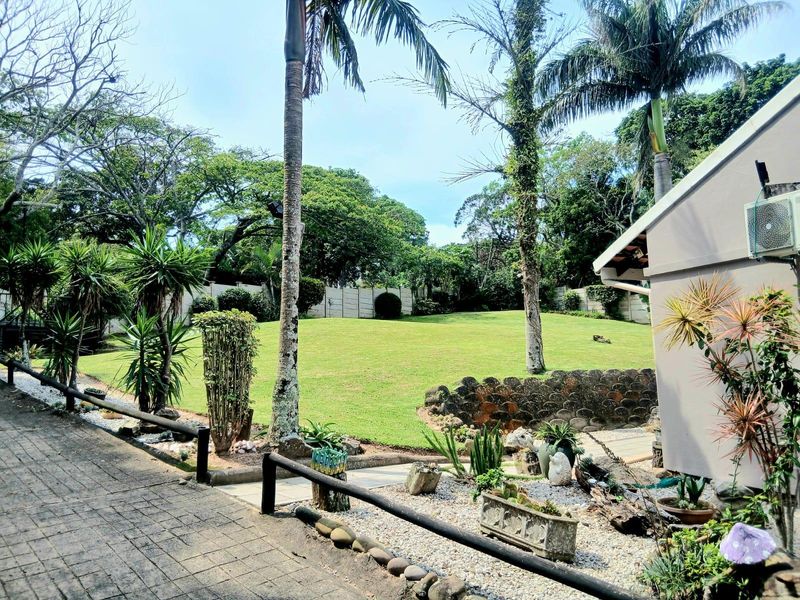 A well-maintained garden featuring a spacious lawn, paved walkway, and established landscaping with a retaining wall and exterior building access.