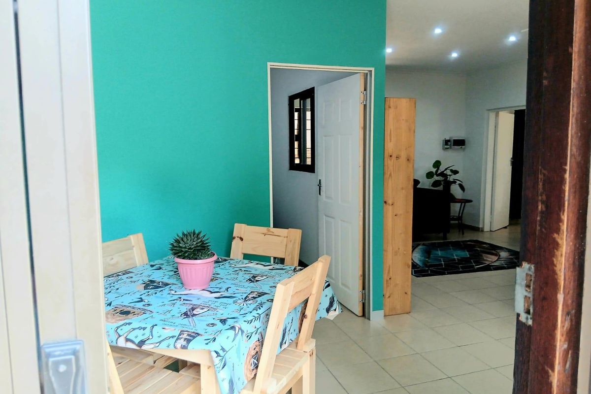 A view into a living area featuring tiled flooring, recessed downlighting, and a bright teal accent wall, leading through to an adjacent room.