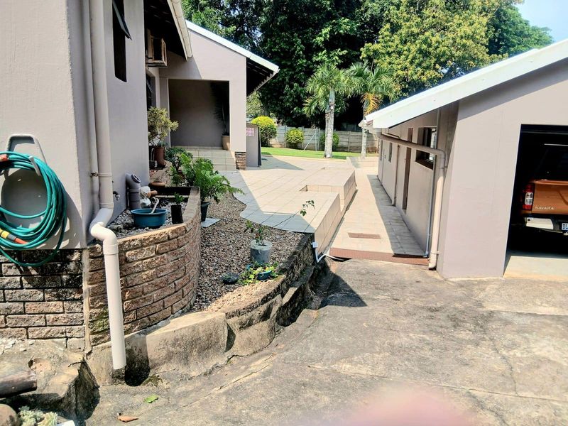 Rear exterior view featuring a paved patio area, brick retaining wall, concrete driveway, and access to the garage.