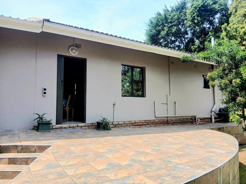 A well-maintained rear exterior view featuring a spacious tiled patio, external wall lighting, and direct access to the interior living space.