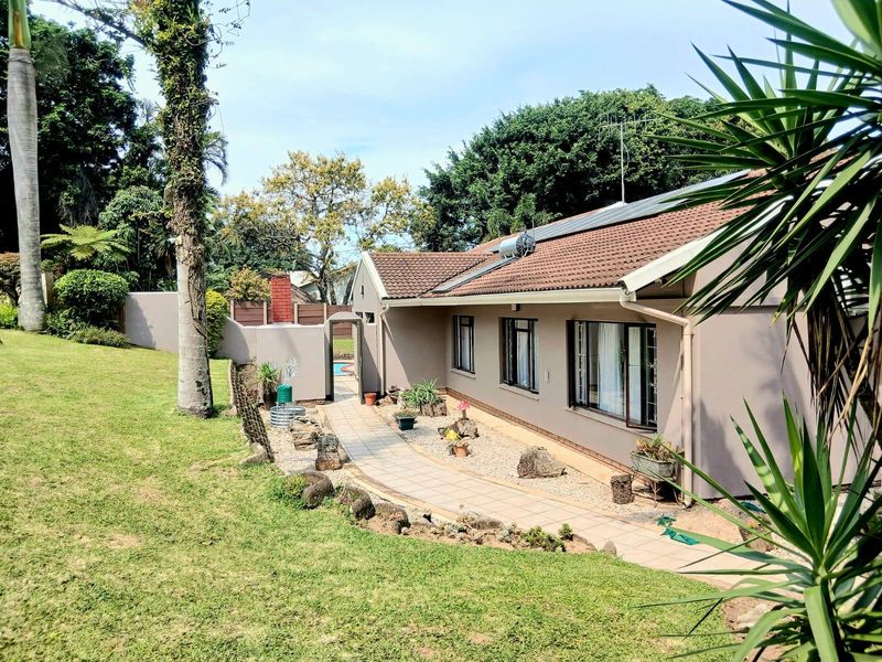 Rear view of the property featuring a tiled roof with solar water heating, a paved walkway, and a well-maintained garden area.