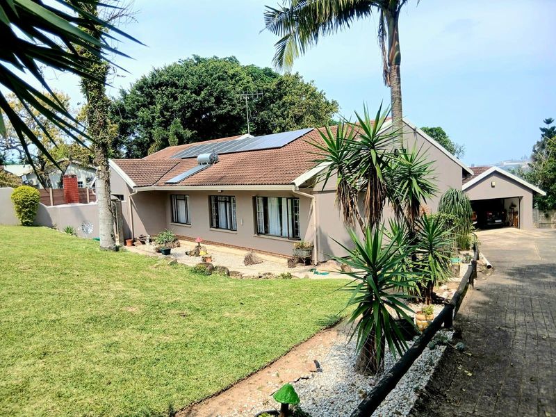 Rear view of the house featuring a tiled roof with solar panels, a solar water heater, a landscaped garden, and a detached garage.