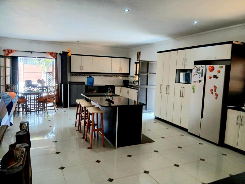 Spacious open-plan kitchen featuring a central island, extensive built-in cabinetry, and tiled flooring, seamlessly connecting to the outdoor patio area.