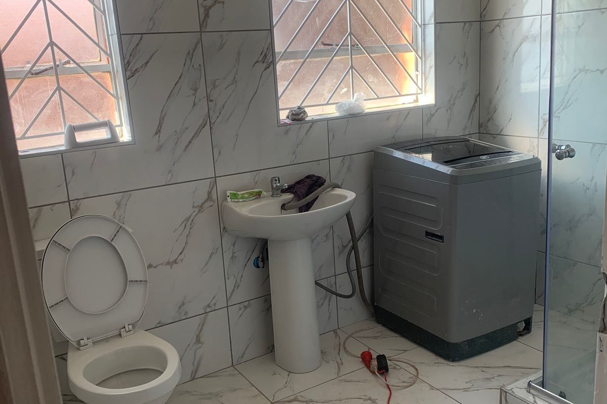 A functional bathroom featuring marble-look wall and floor tiles, a pedestal basin, toilet, and a glass-enclosed shower.