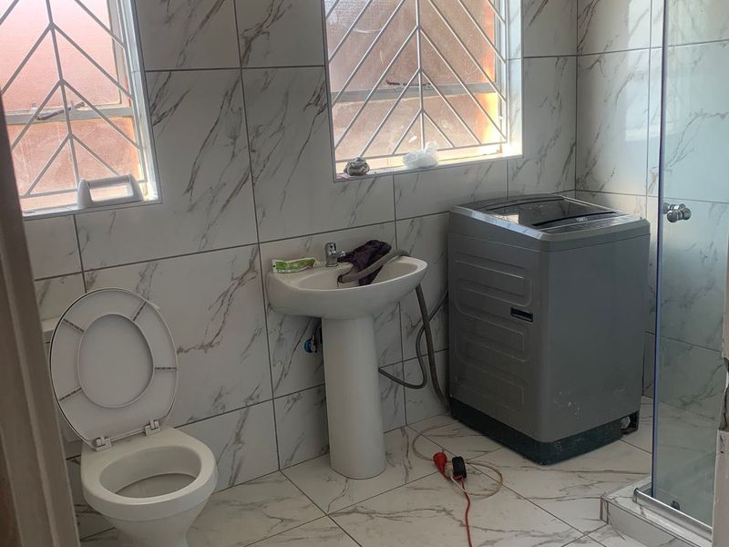 A functional bathroom featuring marble-look wall and floor tiles, a pedestal basin, toilet, and a glass-enclosed shower.