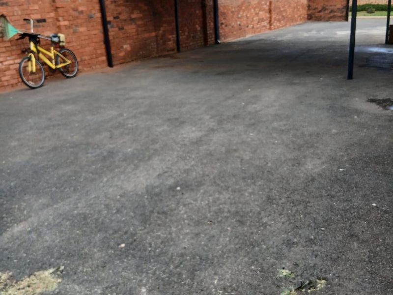 An outdoor carport area featuring a metal structure and brick boundary walls with an asphalt driveway surface.