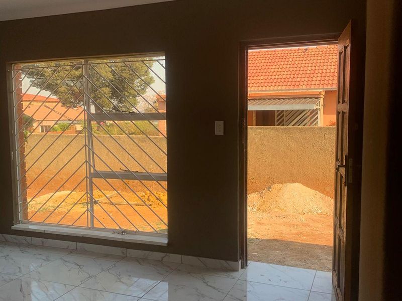 An empty living room featuring polished marble-look floor tiles, recessed lighting, and direct access to the rear yard through a timber door.