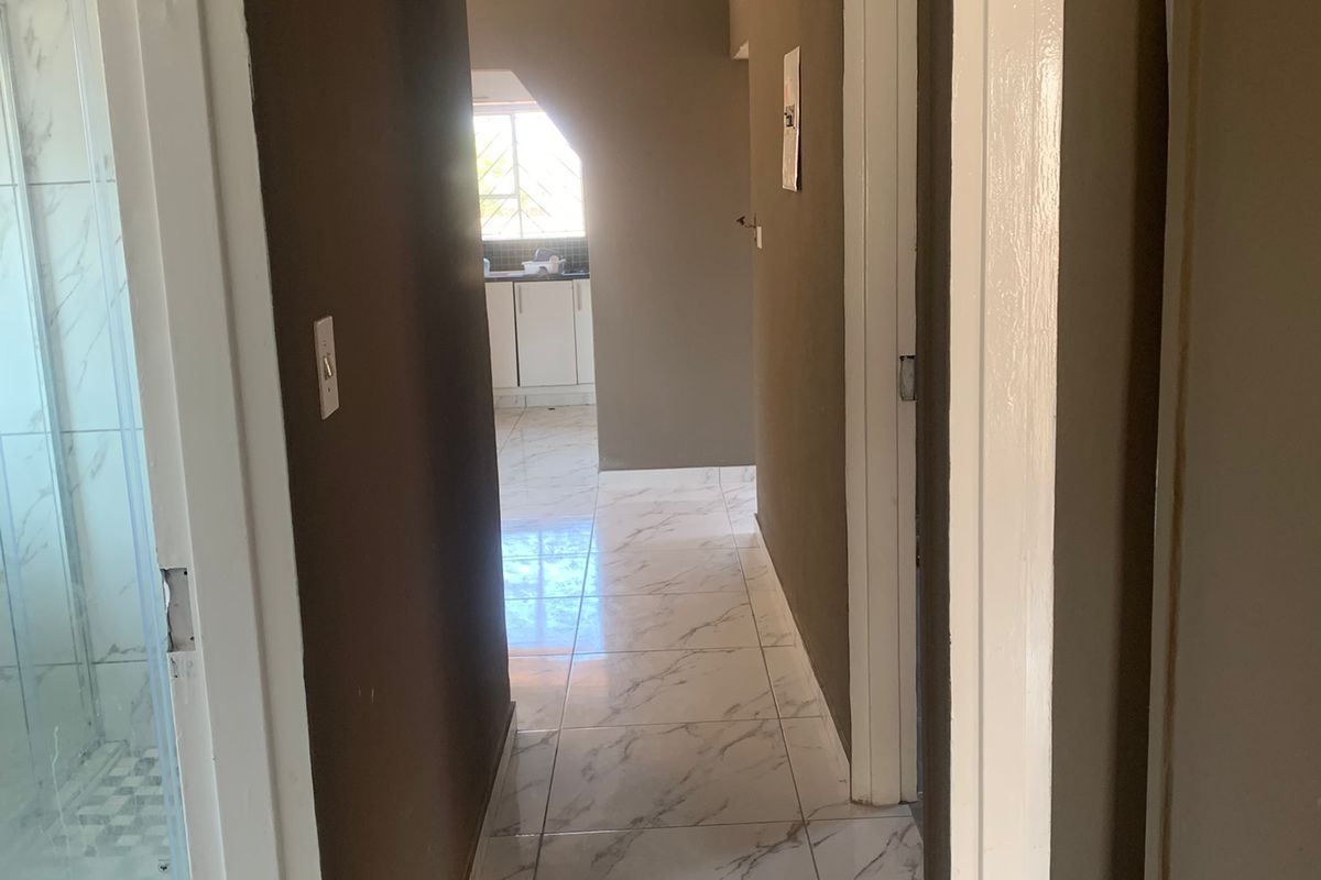 A bright hallway featuring modern marble-look floor tiles, recessed downlighting, and neutral wall finishes, providing access to adjacent rooms.
