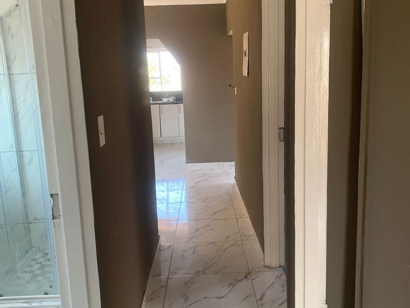 A bright hallway featuring modern marble-look floor tiles, recessed downlighting, and neutral wall finishes, providing access to adjacent rooms.