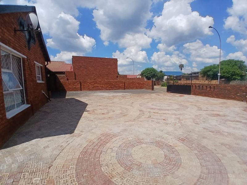Spacious front exterior area featuring decorative brick paving, a secure boundary wall, and a metal driveway gate.